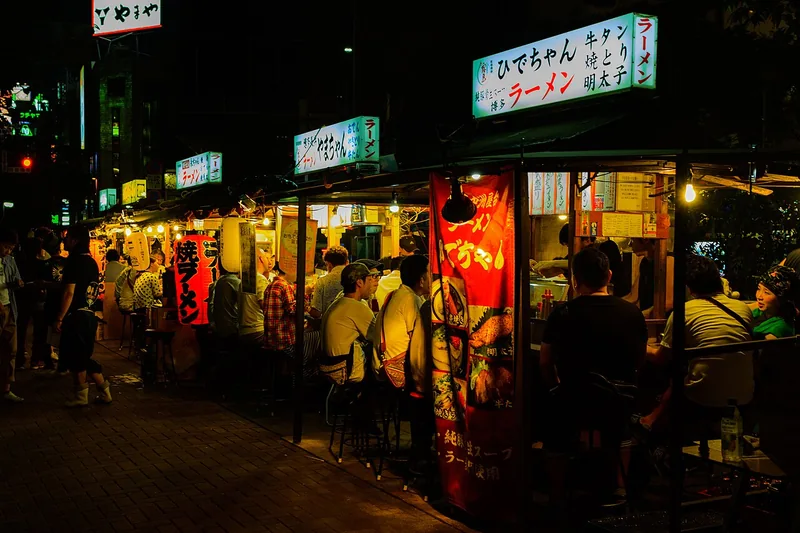 People eating at warmly lit Nakasu yatai food stalls after dark