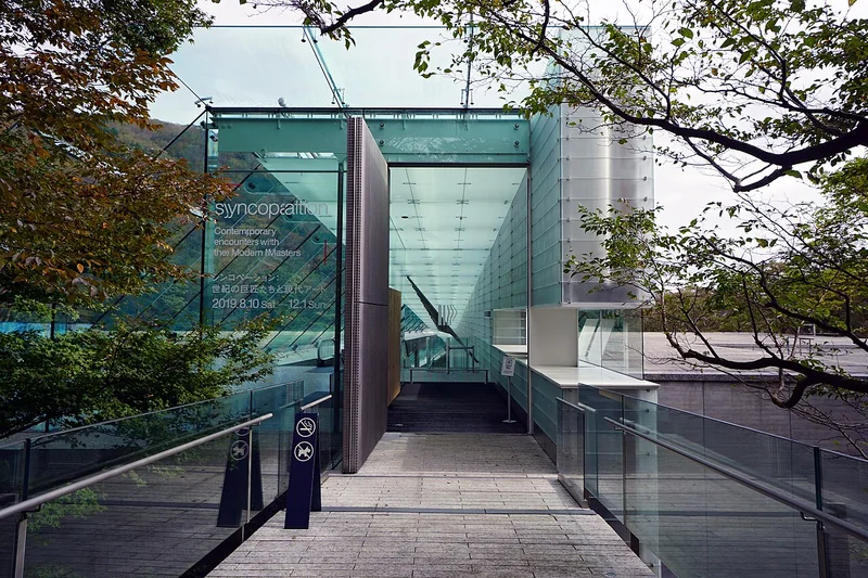 A glass entrance walkway framed by trees at Pola Museum of Art