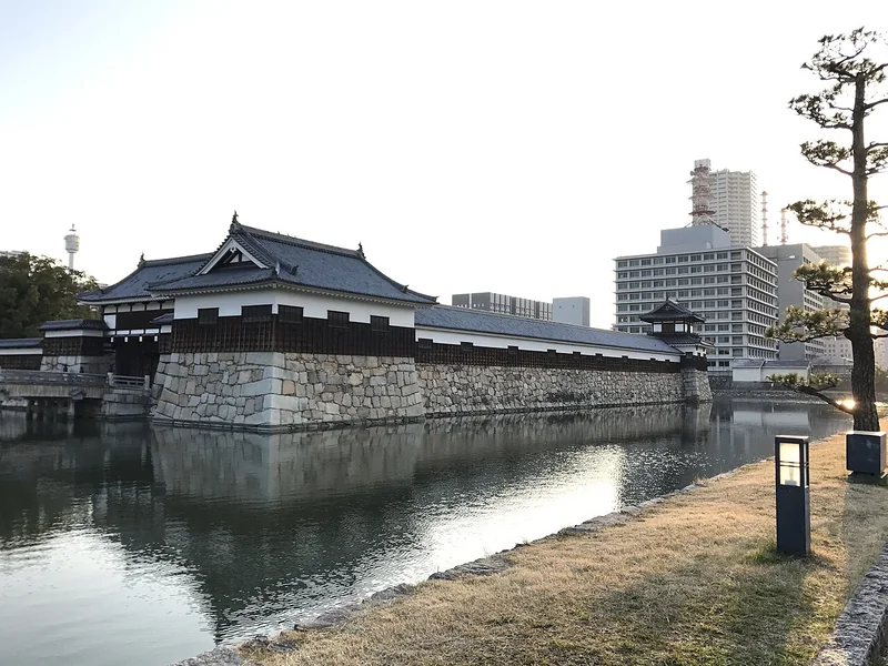 White turrets and stone walls reflected in the moat at Hiroshima Castle