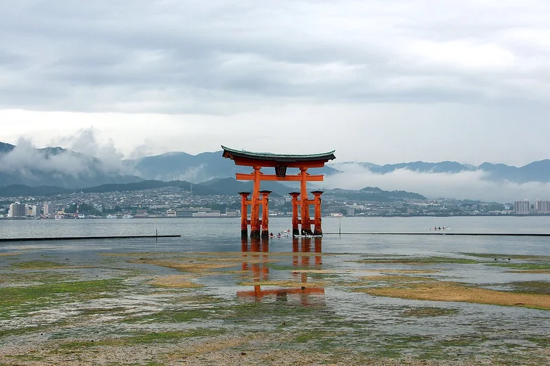 The vermilion torii of Itsukushima Shrine at low tide with misty mountains beyond
