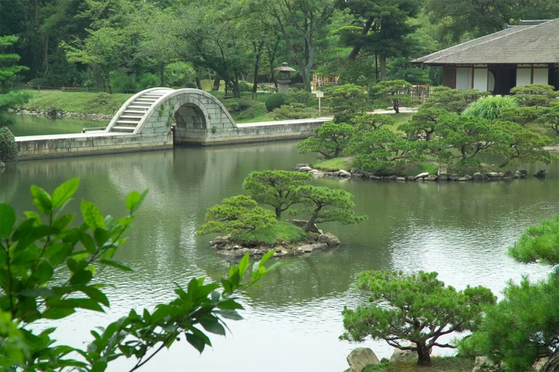 The curved stone bridge and green trees reflected in the pond at Shukkeien Garden