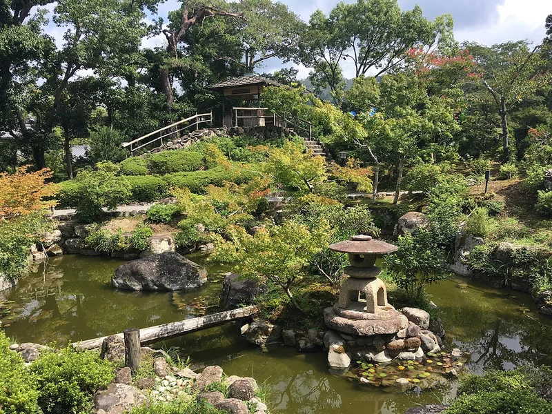 A stone lantern, pond and hillside planting in Yoshikien Garden
