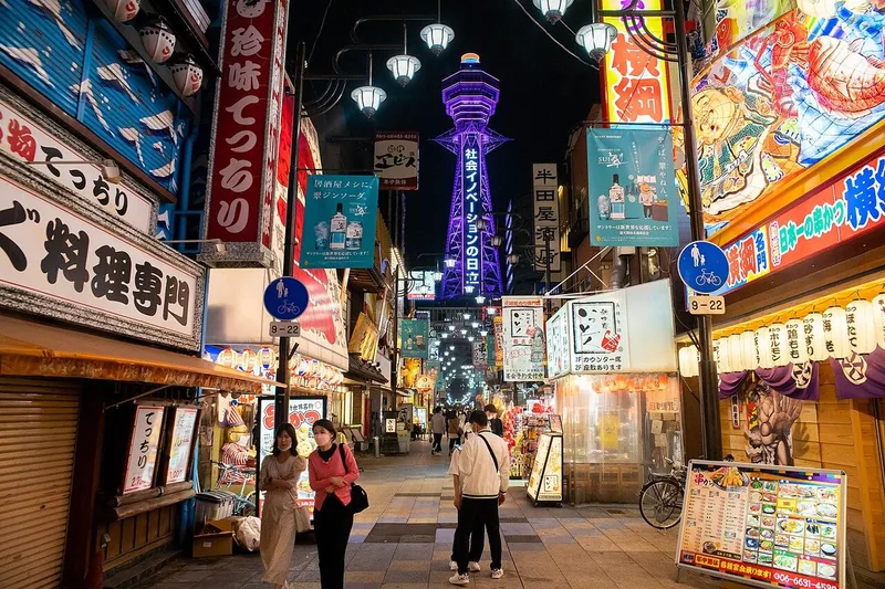 Colourful restaurant signs and Tsutenkaku Tower illuminated in Shinsekai