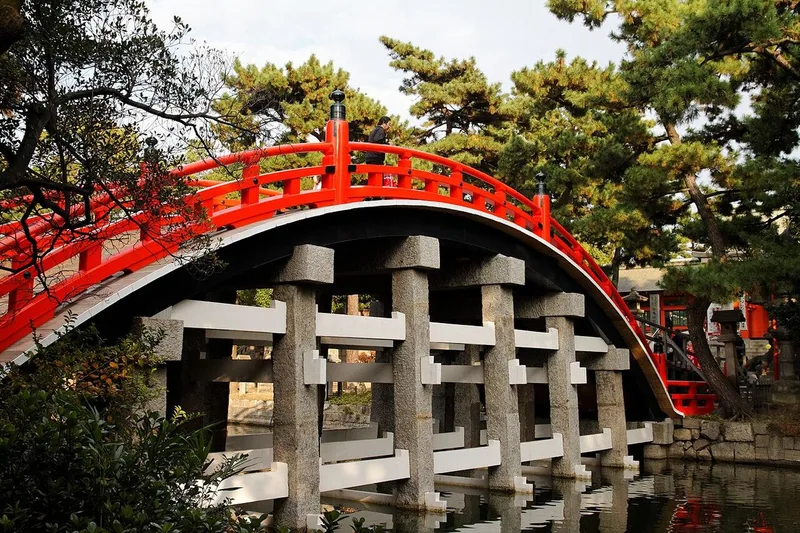 The steep red Sorihashi bridge among trees at Sumiyoshi Taisha