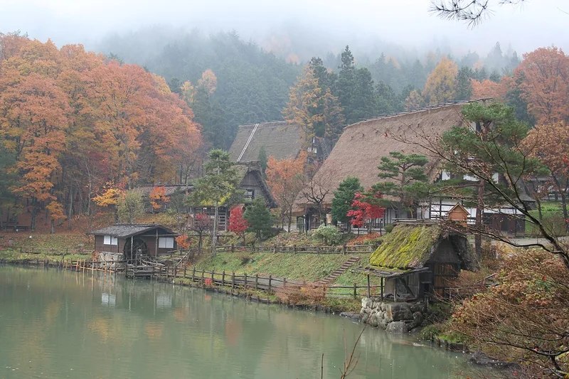 Thatched houses and autumn trees beside the pond at Hida Folk Village