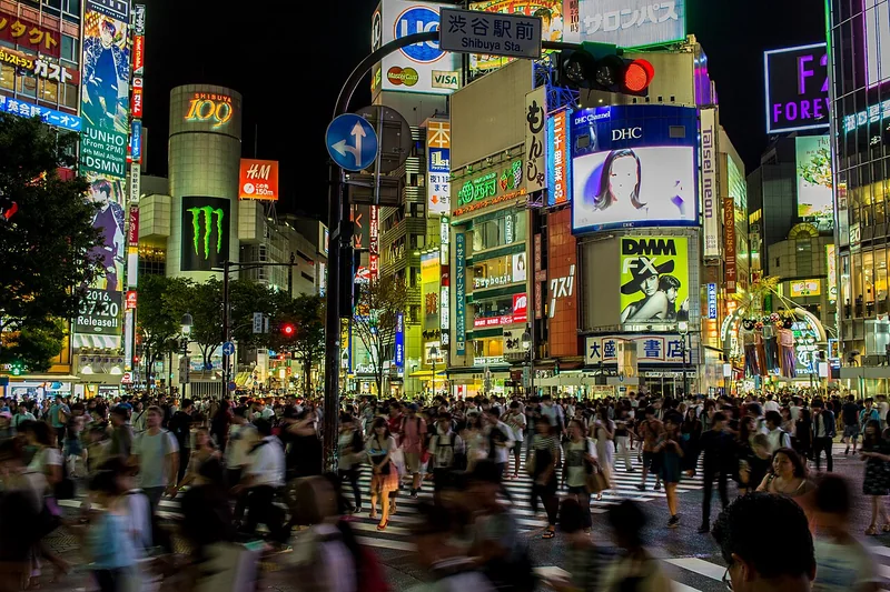 Crowds crossing Shibuya Scramble Crossing beneath bright advertising screens at night