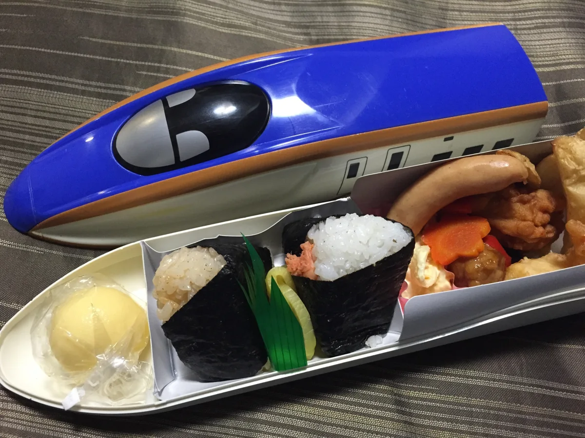 A train-shaped ekiben box with rice snacks and side dishes.