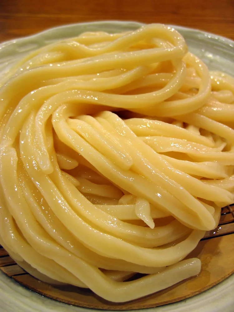 Thick udon noodles on a serving basket.