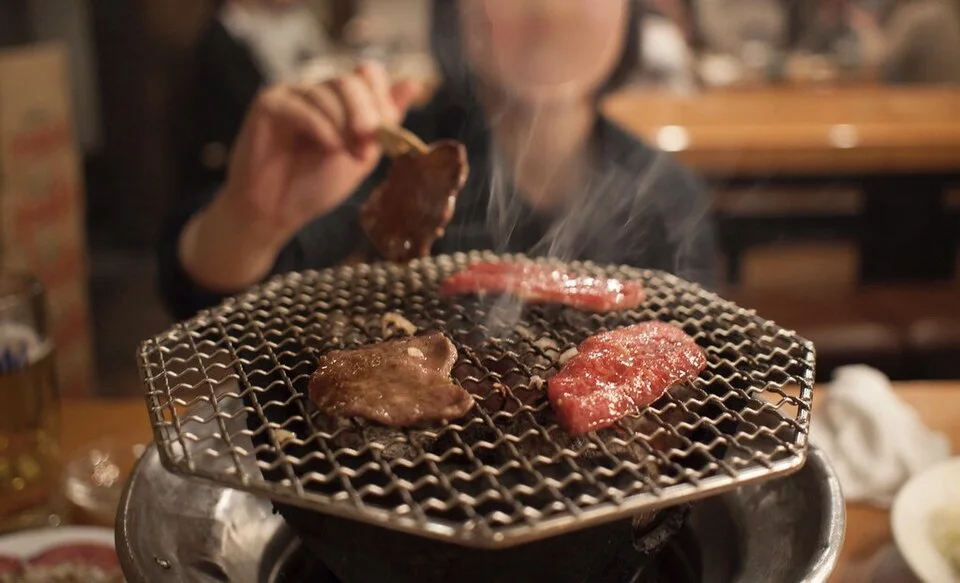 Small pieces of meat cooking on a table grill.