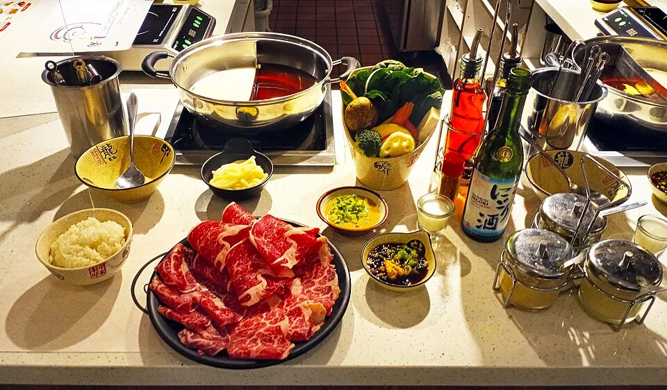 A shabu-shabu spread with raw meat, vegetables and a divided cooking pot.