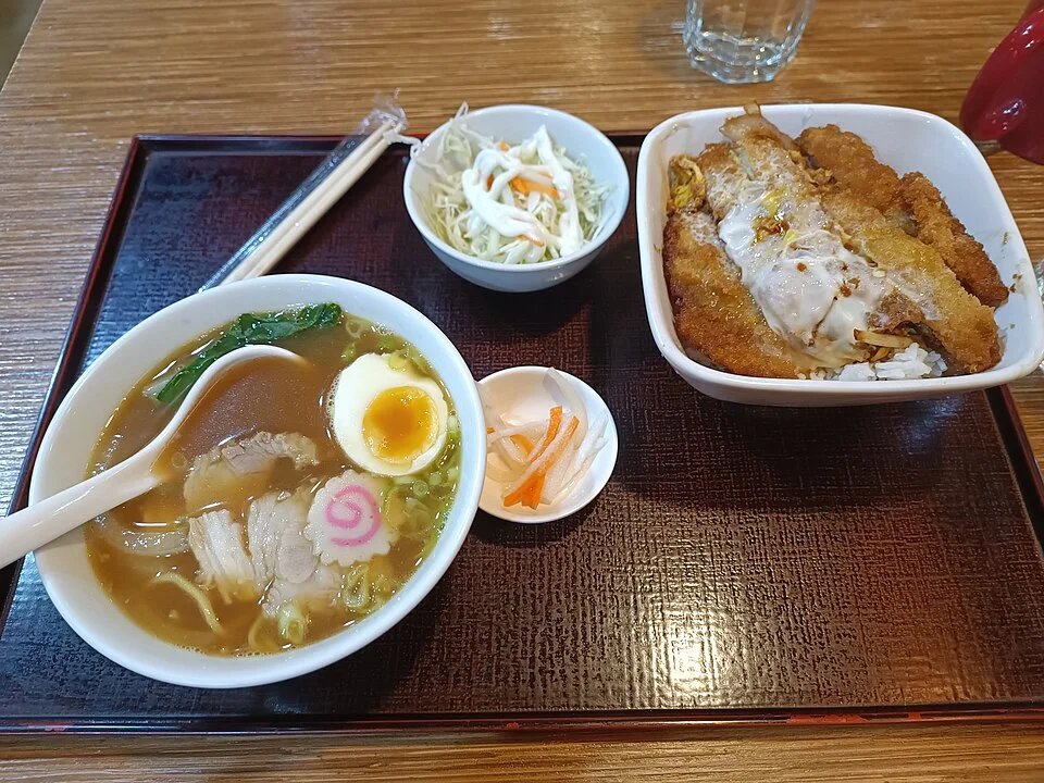 A katsudon rice bowl accompanied by noodles and small sides.